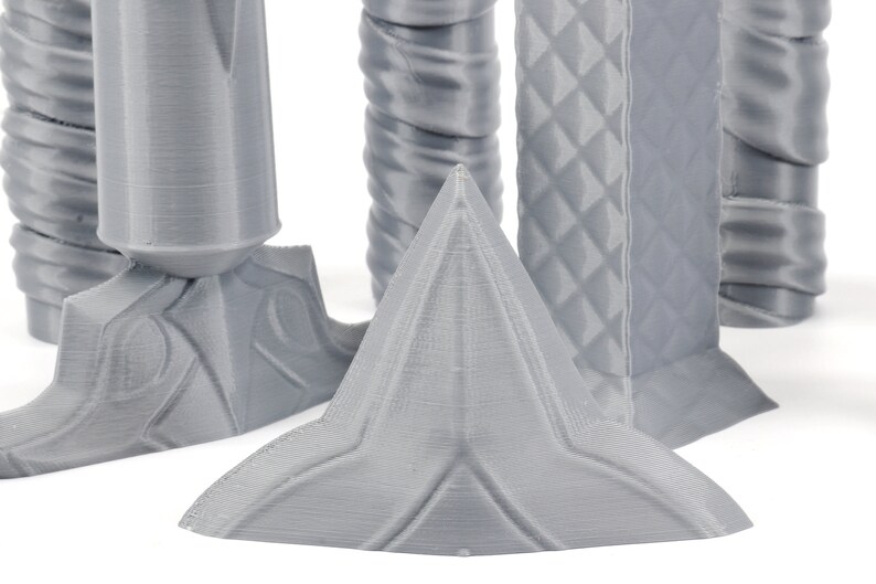 Puede incluir: Primer plano de una forma geom&eacute;trica gris, impresa en 3D, con una parte superior puntiaguda y una base en forma de estrella. La forma est&aacute; hecha de un material liso, similar al pl&aacute;stico.
