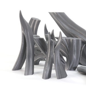 May include: A group of abstract sculptures made of gray 3D printed plastic. The sculptures are arranged in a cluster on a white surface. The sculptures are all different shapes and sizes, but they all have a similar organic, flowing design.