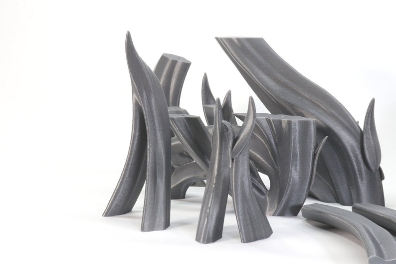 May include: A group of abstract sculptures made of gray 3D printed plastic. The sculptures are arranged in a cluster on a white surface. The sculptures are all different shapes and sizes, but they all have a similar organic, flowing design.