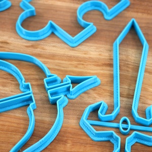 May include: A set of blue plastic cookie cutters shaped like a sword, bow and arrow, and other fantasy-themed shapes.