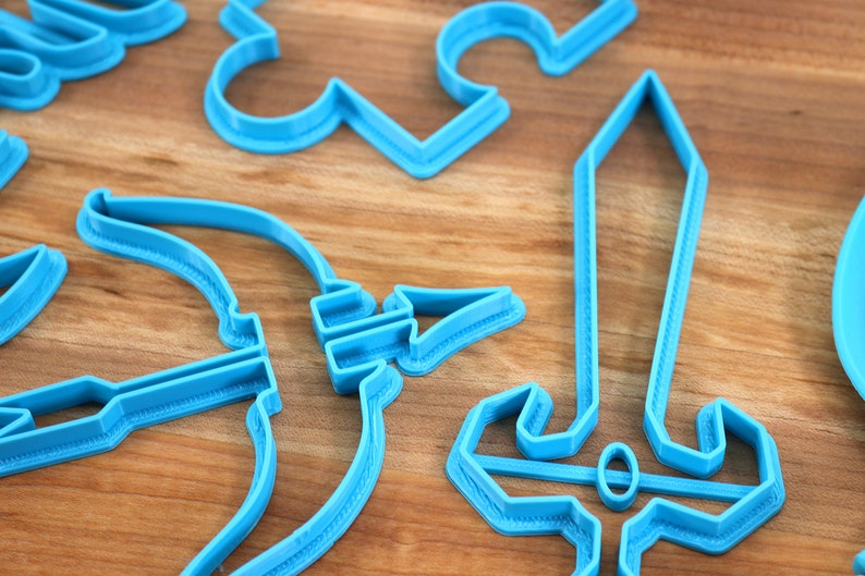 May include: A set of blue plastic cookie cutters shaped like a sword, bow and arrow, and other fantasy-themed shapes.
