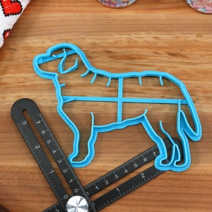 Peut inclure: Emporte-pi&egrave;ce en plastique bleu en forme de chien avec un motif quadrill&eacute; sur le corps. L'emporte-pi&egrave;ce est sur une surface en bois avec une r&egrave;gle.