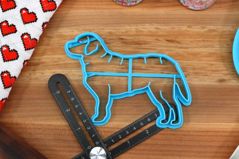 Peut inclure: Emporte-pi&egrave;ce en plastique bleu en forme de chien avec un motif quadrill&eacute; sur le corps. L'emporte-pi&egrave;ce est sur une surface en bois avec une r&egrave;gle.