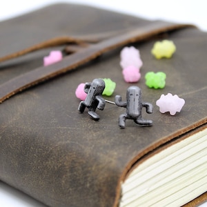 May include: Two small, silver-colored figurines of a running character on a brown leather journal with colorful candy sprinkles scattered around them.