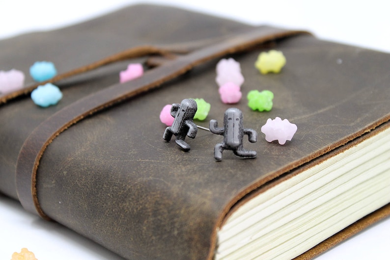 May include: Two small, silver-colored figurines of a running character on a brown leather journal with colorful candy sprinkles scattered around them.
