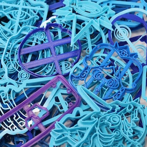 Op de afbeelding: Een close-up van een stapel blauwe en paarse plastic koekjesvormen. De vormen zijn in verschillende vormen, waaronder een hart, een ster en een cirkel.