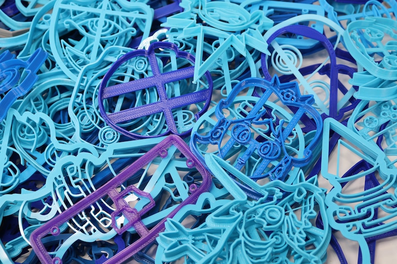 Op de afbeelding: Een close-up van een stapel blauwe en paarse plastic koekjesvormen. De vormen zijn in verschillende vormen, waaronder een hart, een ster en een cirkel.
