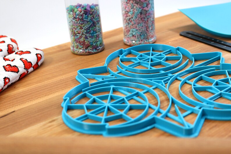 May include: Blue plastic cookie cutters shaped like a snowflake with a circular design. The cutters are on a wooden surface.