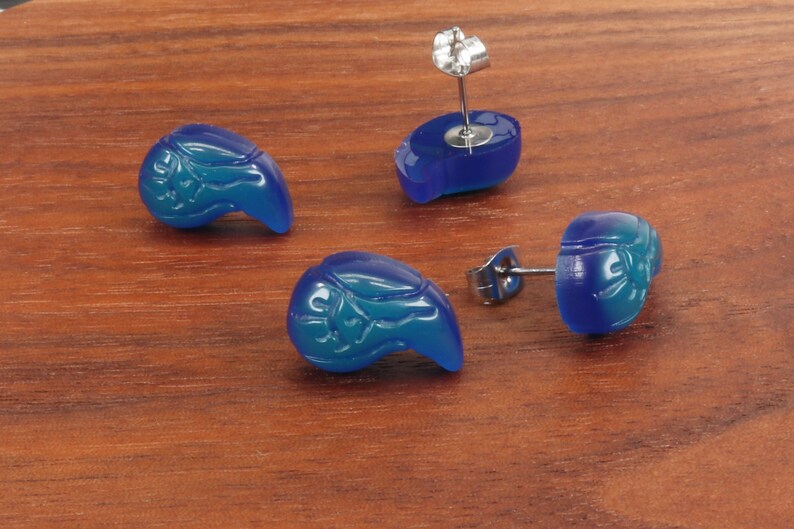May include: A pair of blue teardrop-shaped earrings with a carved design. The earrings have silver posts and backs.