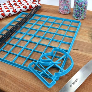 May include: A blue plastic baking mat with a grid pattern, a blue plastic cookie cutter shaped like the number 13, and a blue plastic spatula with a silver handle. The spatula has the word "Wilton" printed on the handle.