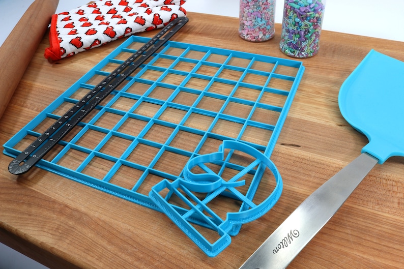 May include: A blue plastic baking mat with a grid pattern, a blue plastic cookie cutter shaped like the number 13, and a blue plastic spatula with a silver handle. The spatula has the word "Wilton" printed on the handle.
