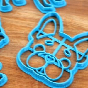 Puede incluir: Un cortador de galletas de pl&aacute;stico azul con forma de cabeza de perro. El cortador tiene un dise&ntilde;o detallado de la cara del perro, incluyendo la nariz, los ojos y las orejas.