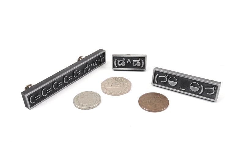 May include: Three silver metal pins with different symbols. The first pin has the text "C=C=C=C=C= r(&bull;&omega;&bull;)". The second pin has the text "(^)". The third pin has the text "づ".