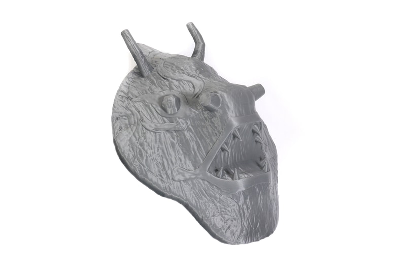 Puede incluir: Una m&aacute;scara gris impresa en 3D con un dise&ntilde;o detallado de una criatura con dientes afilados y cuernos. La m&aacute;scara tiene una superficie texturizada y parece estar hecha de pl&aacute;stico.