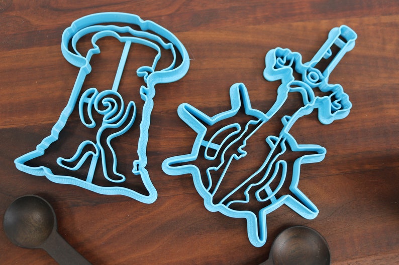 Puede incluir: Dos cortadores de galletas de pl&aacute;stico azul, uno con forma de persona y el otro con forma de espada.