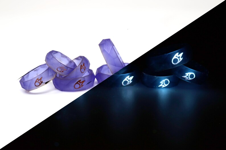 May include: A set of six purple glow-in-the-dark rings with a red flame design. The rings are stacked on a white surface and glow brightly in the dark.