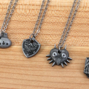 May include: Four silver necklaces with different pendants: an ocarina, a shield with a triforce symbol, a Majora's Mask, and a stone with a swirl design.