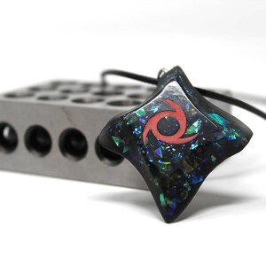 Pu&ograve; includere: Un ciondolo a forma di stella nera con un design a spirale rosso e glitter iridescente incorporato nella resina. Il ciondolo &egrave; attaccato a un cordino nero.