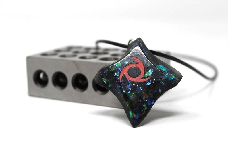 Pu&ograve; includere: Un ciondolo a forma di stella nera con un design a spirale rosso e glitter iridescente incorporato nella resina. Il ciondolo &egrave; attaccato a un cordino nero.