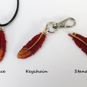 May include: Three red and gold feather charms, one on a black cord necklace, one on a silver keychain, and one on a silver jump ring. The charms are labeled "Necklace", "Keychain", and "Standard".