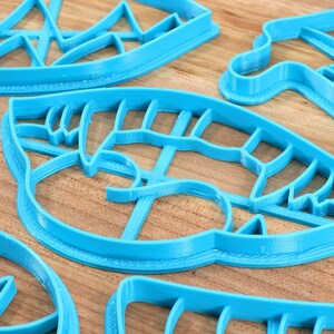 May include: A set of five blue plastic cookie cutters in various shapes, including a leaf, a mountain range, and a geometric design.