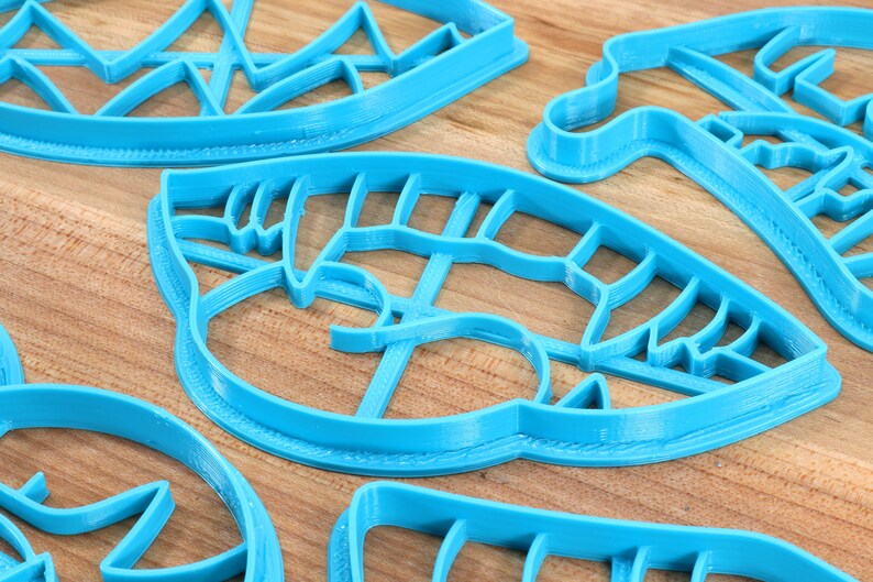 May include: A set of five blue plastic cookie cutters in various shapes, including a leaf, a mountain range, and a geometric design.