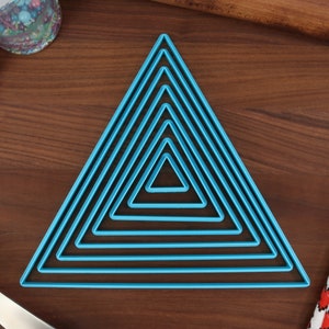 May include: A set of nine blue triangle-shaped cookie cutters of varying sizes. The cutters are arranged in a pyramid shape on a wooden surface.