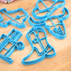 May include: A set of five blue plastic cookie cutters shaped like a cowboy boot, a cowboy hat, a longhorn skull, a wagon, and the state of Texas.