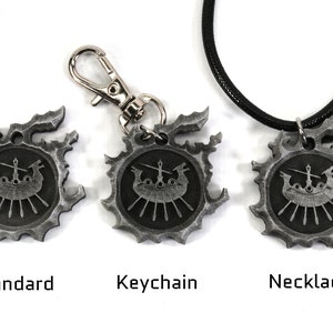 Op de afbeelding: Drie zilverkleurige metalen hangers met een gestileerd schipontwerp. De hangers zijn verkrijgbaar als standaardstuk, sleutelhanger en ketting.