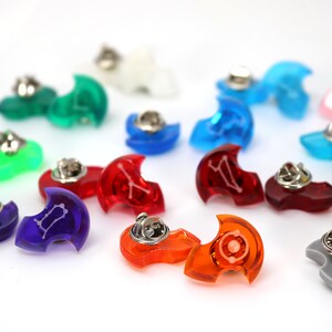 May include: A collection of colorful, crescent-shaped pins with zodiac symbols. The pins are made of clear plastic and have a silver pin back.
