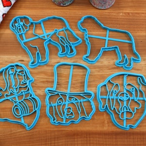 May include: A collection of blue plastic dog-shaped cookie cutters. The cutters depict various dog breeds in different poses, including standing and sitting. A rolling pin, spatula, and heart-patterned cloth are also visible.