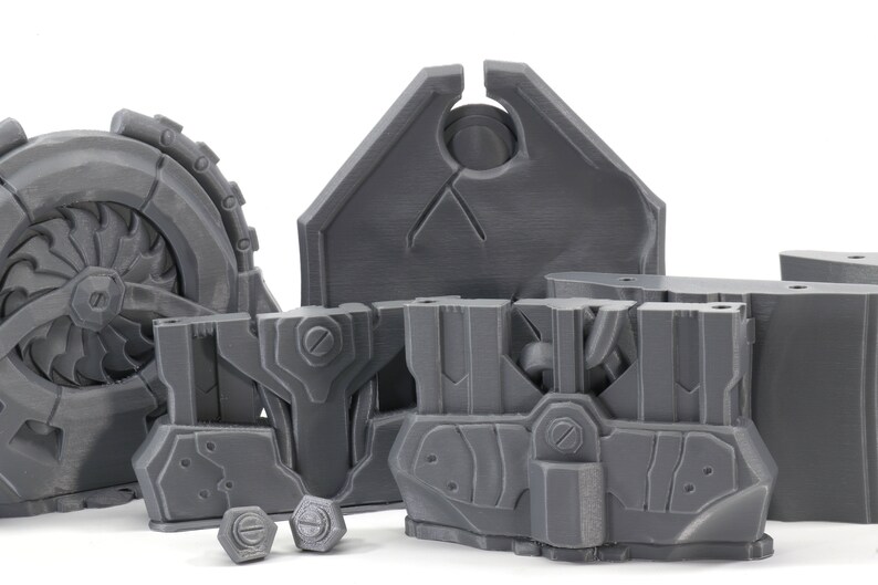 May include: A set of gray 3D printed plastic pieces for a model kit. The pieces include a large wheel with a fan, a shield, and several smaller pieces.