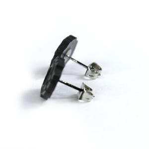 May include: A pair of black stud earrings with a simple design. The earrings are made of a smooth, matte material and have a silver post.