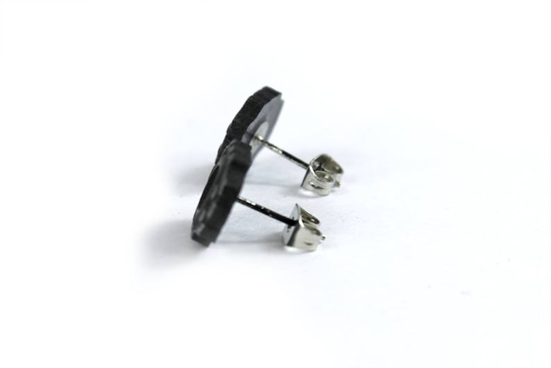 May include: A pair of black stud earrings with a simple design. The earrings are made of a smooth, matte material and have a silver post.