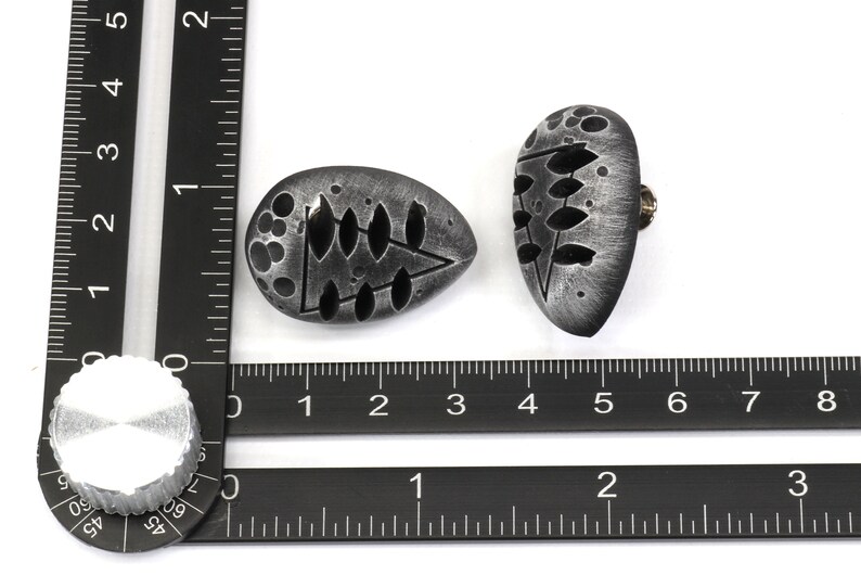 May include: Two silver-colored, oval-shaped, decorative knobs with a black and white design. The knobs have a textured surface and a small screw on the back.