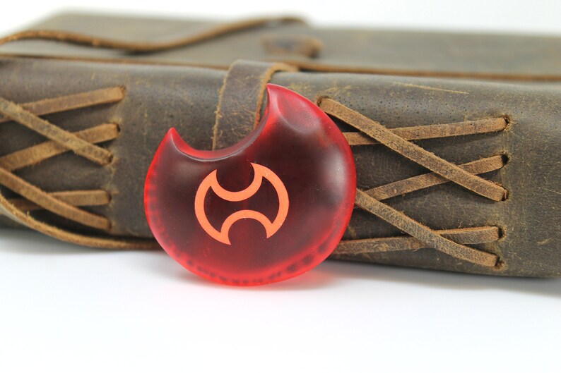 May include: A red, crescent-shaped pendant with a stylized orange symbol. The pendant is made of glass and has a smooth, glossy finish.