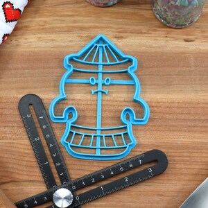 May include: Blue plastic cookie cutter shaped like a carousel with a face and a striped roof.