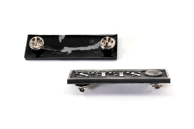 May include: Two black enamel pins with silver metal accents. The first pin is blank and the second pin says "STEF'S" in silver lettering.
