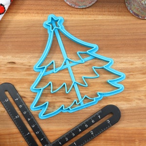 Op de afbeelding: Een blauwe plastic kerstboomkoekjesvormer met een ster bovenop. De vormer ligt op een houten oppervlak.