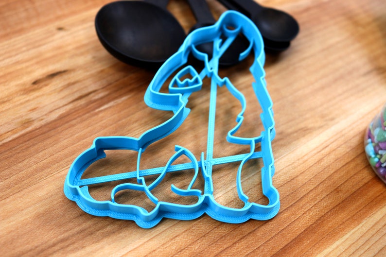 May include: A blue plastic cookie cutter shaped like a dog sitting down. The cutter is on a wooden surface.