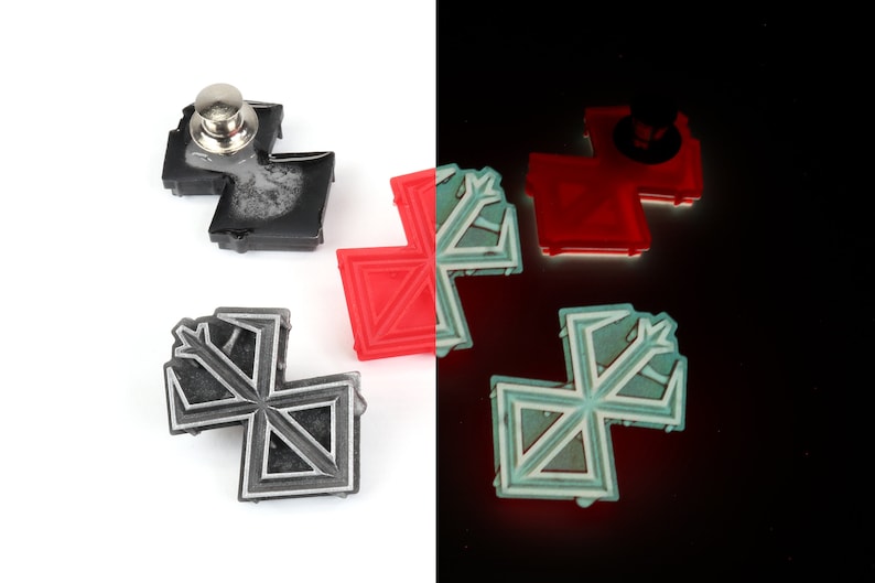 May include: Four black and silver pins with a geometric design. The pins are in the shape of a cross with a pointed tip at the top. The pins are on a white background. One pin has a silver pin back.