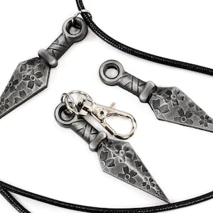 May include: Three silver-colored throwing knives with floral designs, two on a black cord necklace and one on a silver key chain.