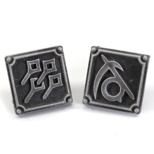 May include: Two silver-toned metal pins with square designs. One pin features a stylized symbol of a scythe and the other pin features a stylized symbol of four squares.