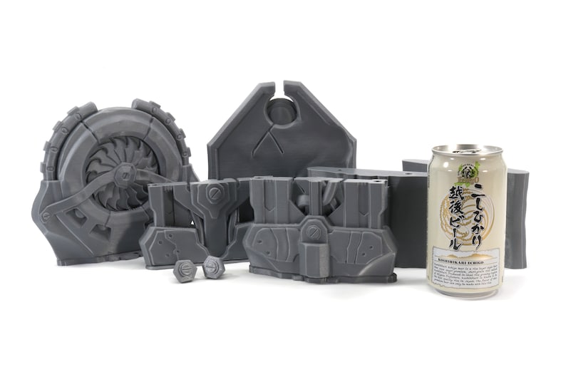 May include: A set of gray 3D printed plastic parts for a model kit. The parts include a large wheel with a fan, a shield with a hole in the center, two smaller parts with intricate details, and two small round pieces. A can of Japanese beer is included for scale.