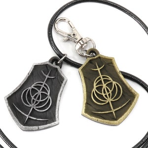 May include: Two silver and gold pendants with a black cord necklace. The pendants are shaped like shields with a circular design and a vertical line in the center.