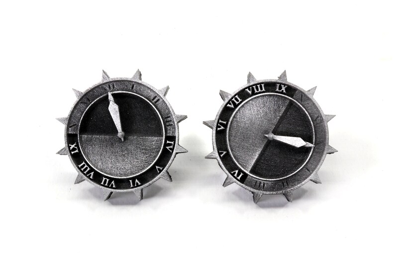 Puede incluir: Dos engranajes de reloj de color plateado con marcas de n&uacute;meros romanos. Los engranajes est&aacute;n divididos a la mitad, con una mitad negra y la otra mitad plateada. Las manecillas del reloj son plateadas y apuntan a diferentes horas.