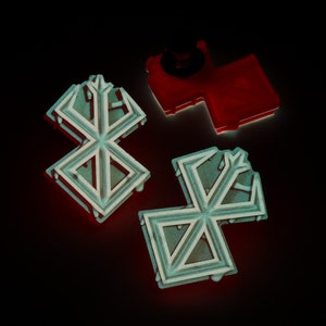 May include: Three decorative metal pins in the shape of a stylised snowflake. Two of the pins are silver with a black outline, and one is red.