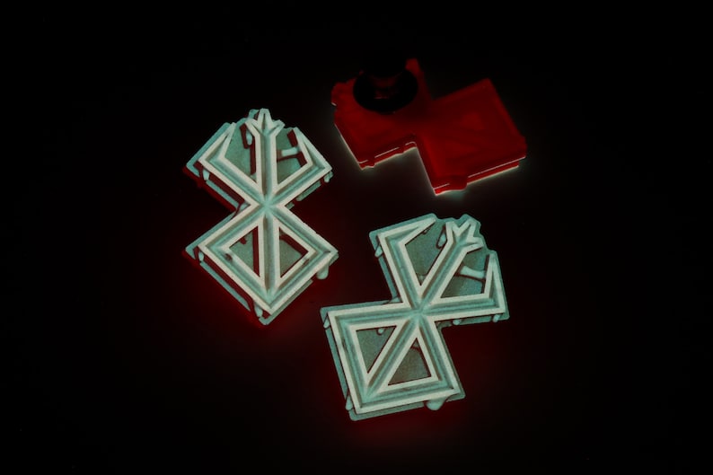 May include: Three decorative metal pins in the shape of a stylised snowflake. Two of the pins are silver with a black outline, and one is red.