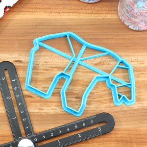 May include: A blue plastic cookie cutter shaped like a geometric animal, possibly a giraffe, on a wooden surface.