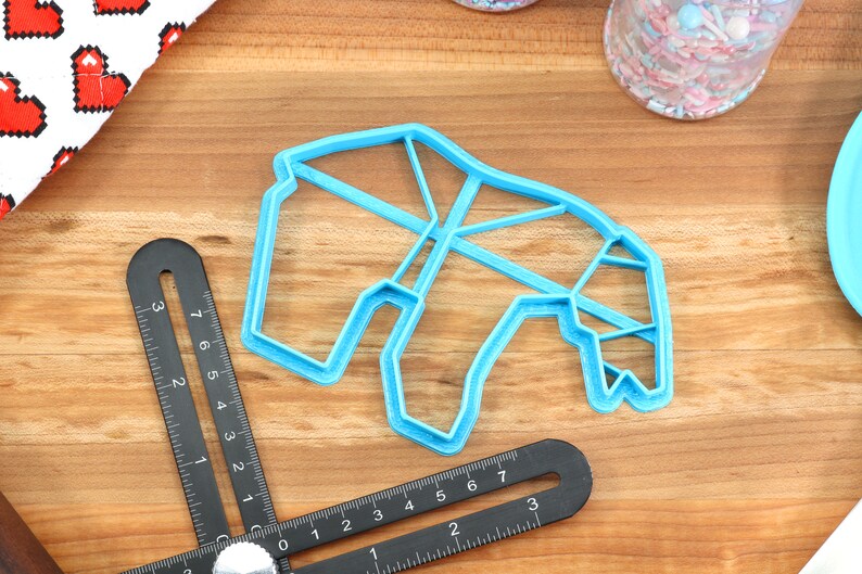 May include: A blue plastic cookie cutter shaped like a geometric animal, possibly a giraffe, on a wooden surface.